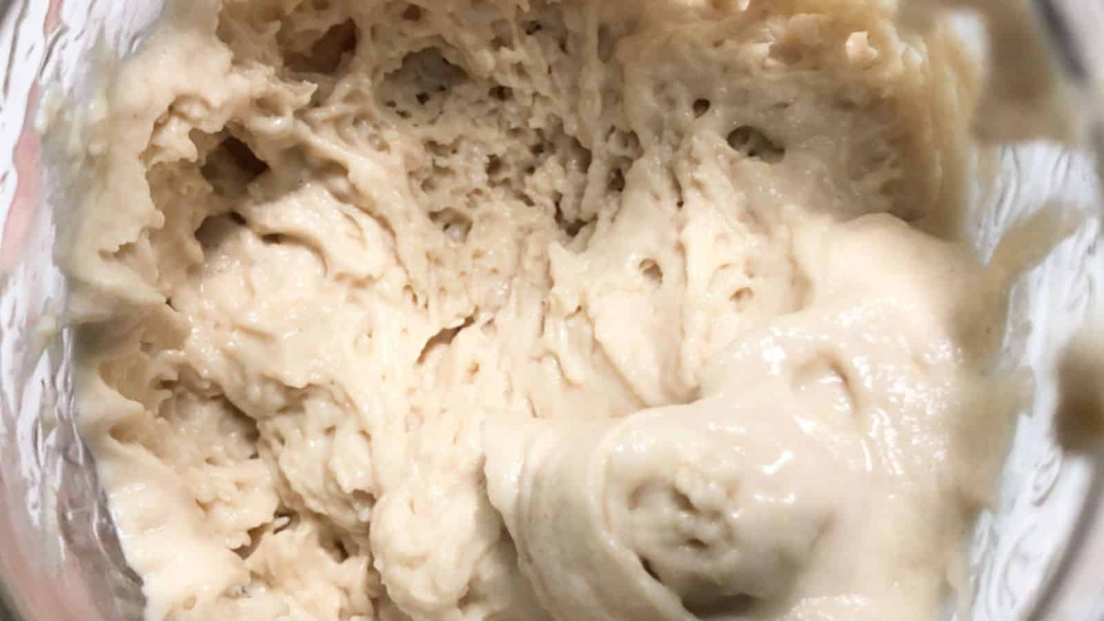 Close-up of creamy, beige-colored dough with an airy texture in a glass container.
