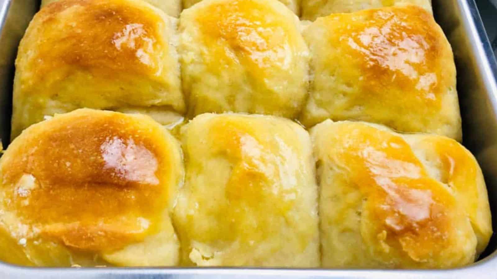 A baking tray filled with nine freshly baked, golden brown, and shiny dinner rolls closely arranged together.