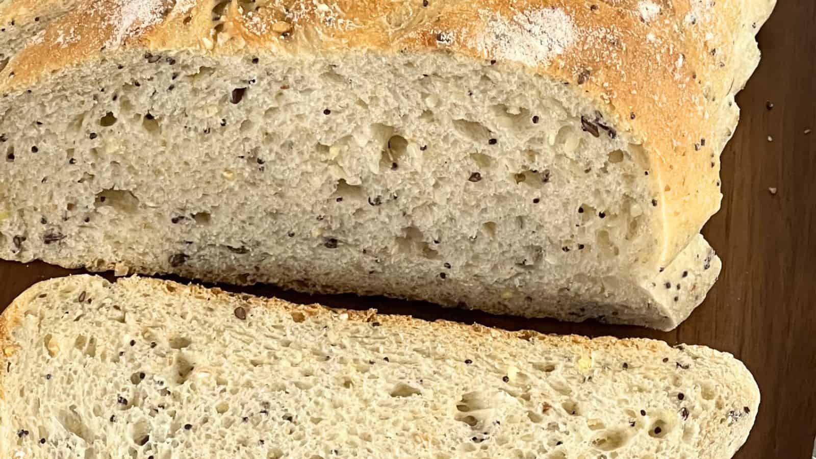 Close-up of a loaf of bread with visible seeds, partially sliced to reveal the texture of the interior crumb.