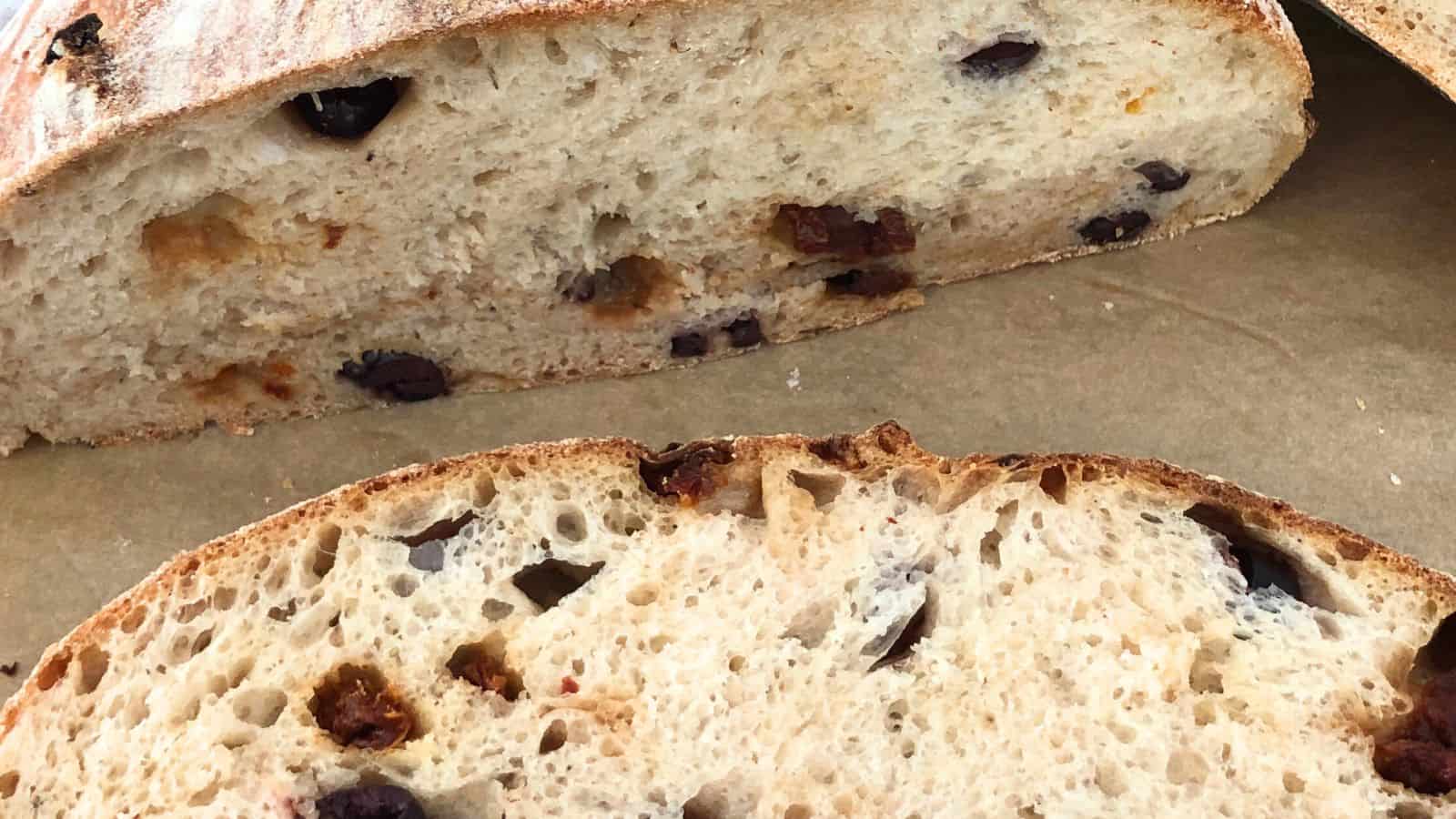 Close-up of sliced olive bread on a cutting board, showing the interior texture and olives embedded in the loaf.
