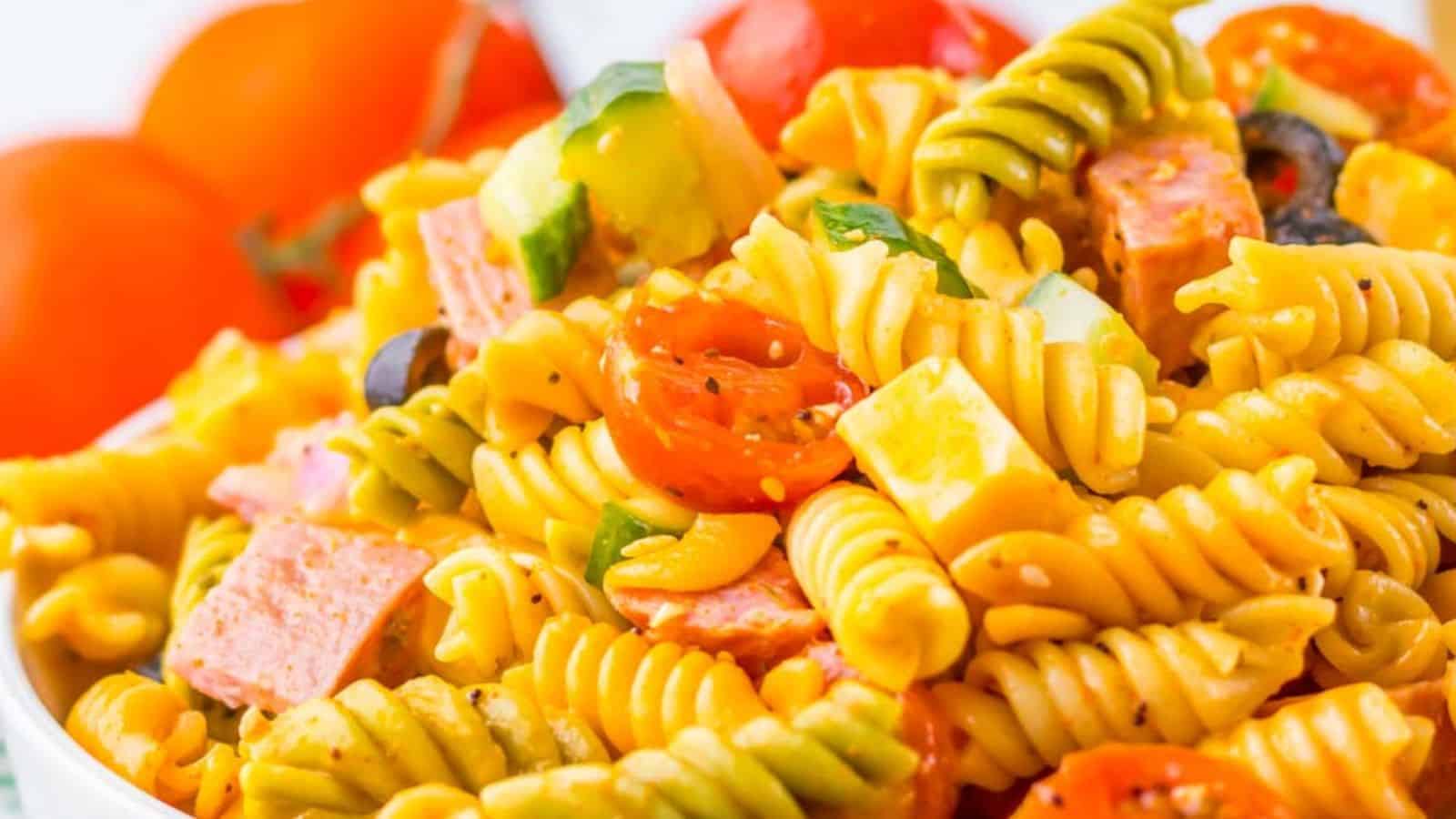 A vibrant pasta salad with fusilli, cherry tomatoes, bell peppers, black olives, and diced salami in a clear bowl.