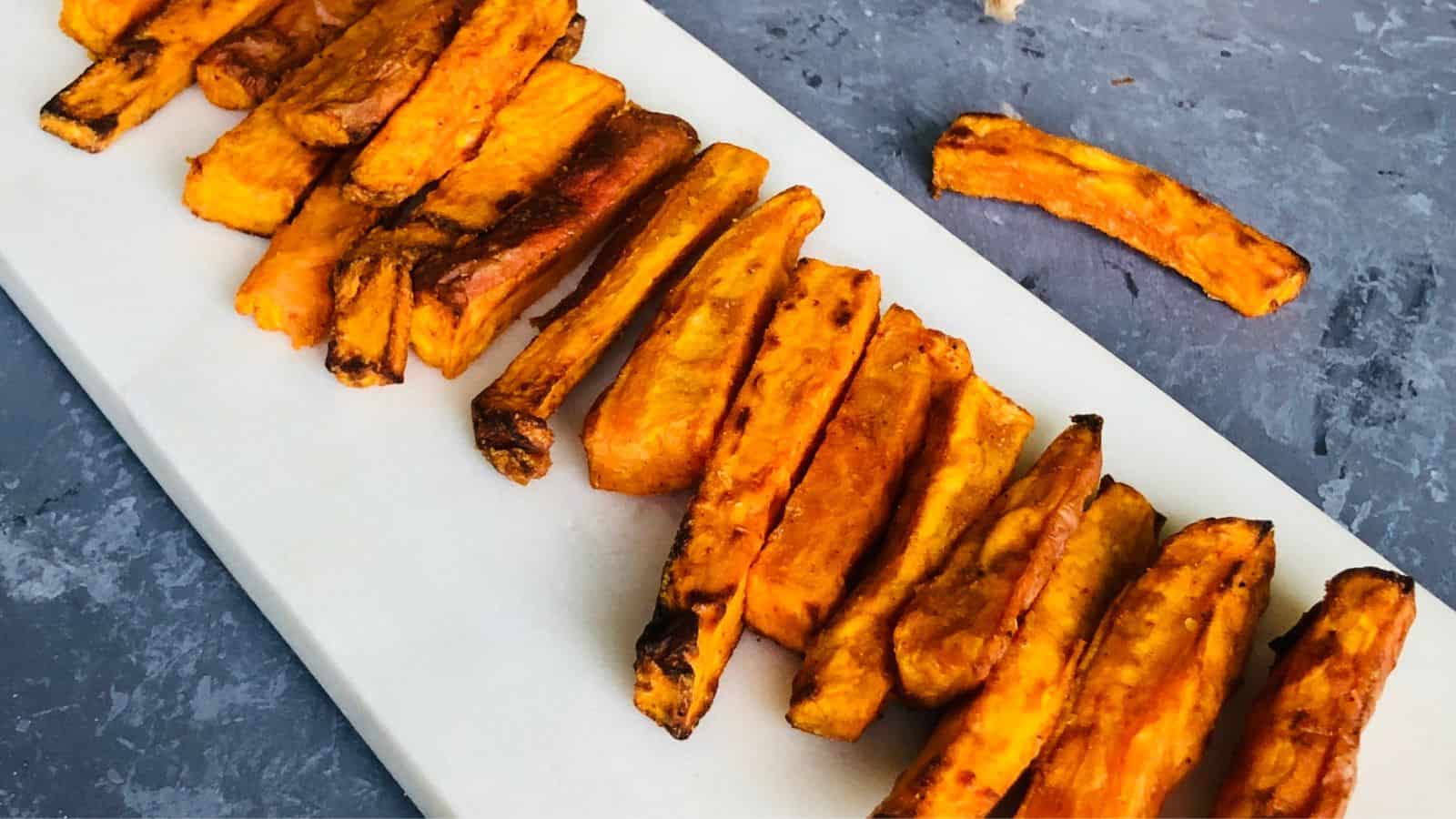 Roasted sweet potato fries arranged neatly on a white rectangular plate, with a dark gray background.