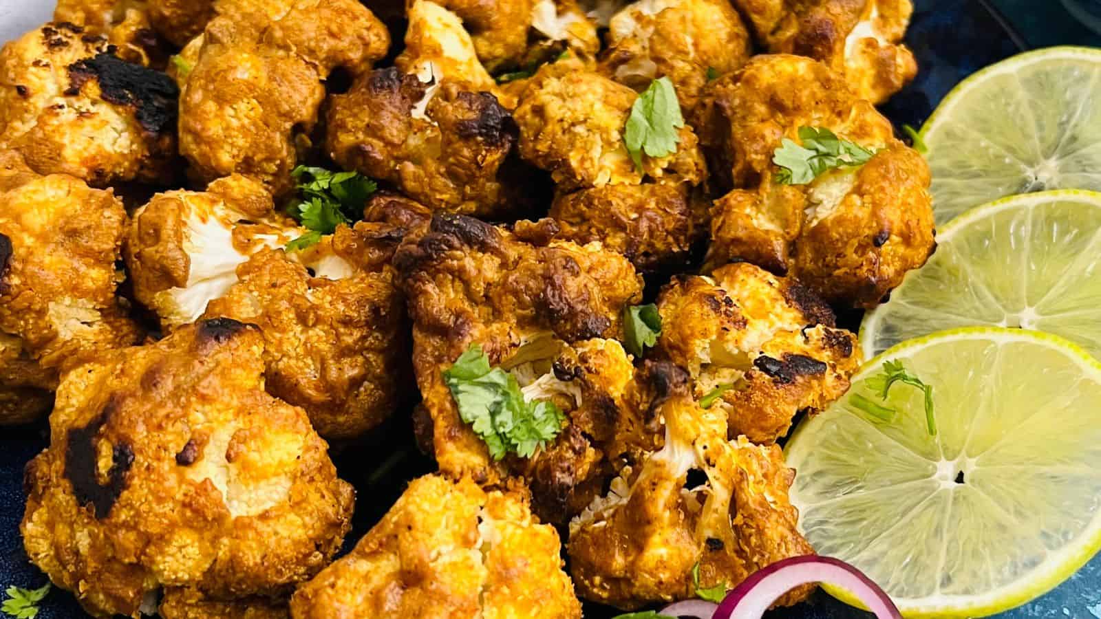 A platter of fried cauliflower bites garnished with lemon slices and fresh cilantro.