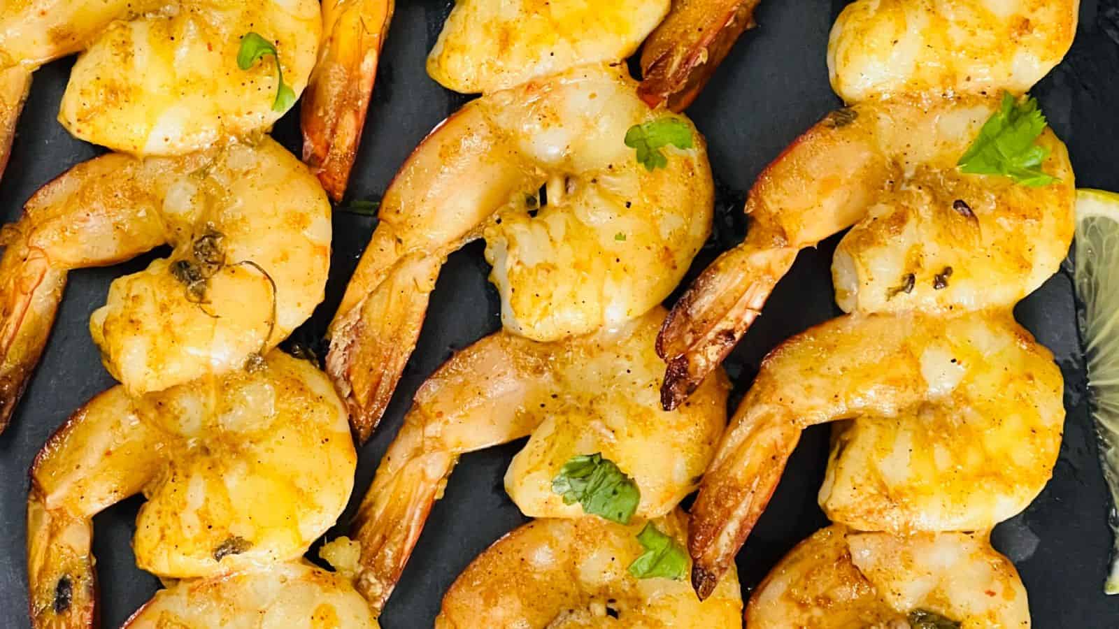 Grilled shrimp skewers seasoned with spices and garnished with fresh herbs, served on a dark plate.