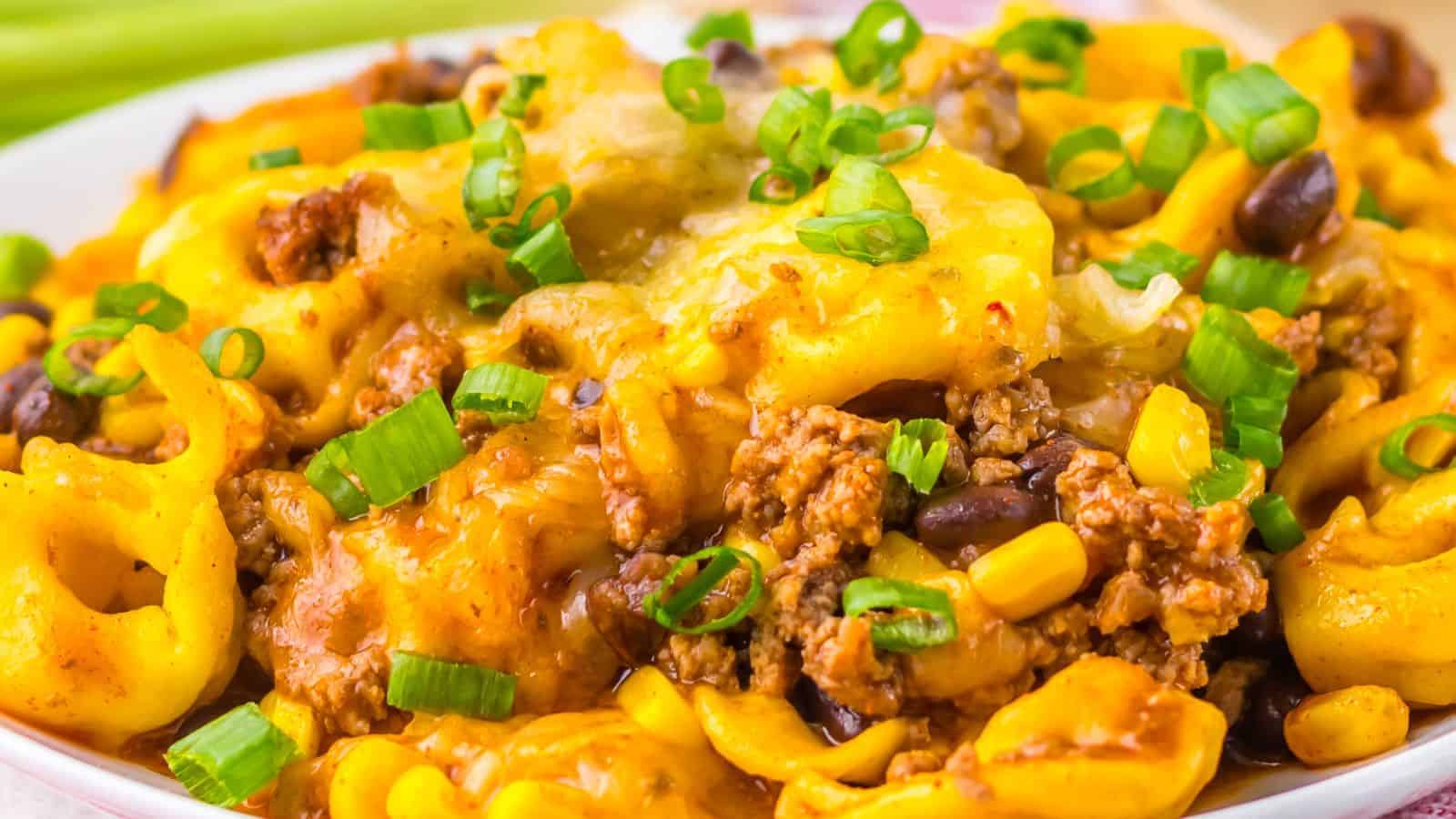 Close-up of a Beef Enchilada Tortellini dish topped with ground meat, corn, black beans, and chopped green onions.