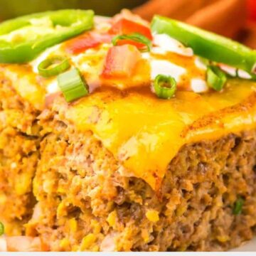 Close-up of a slice of cheesy taco casserole topped with chopped tomatoes, green onions, and jalapeño slices on a white plate, reminiscent of the comforting flavors found in slow cooker taco meatloaf.