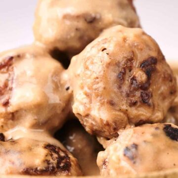 A close-up of Swedish meatballs covered in a creamy sauce, piled in a wooden bowl.