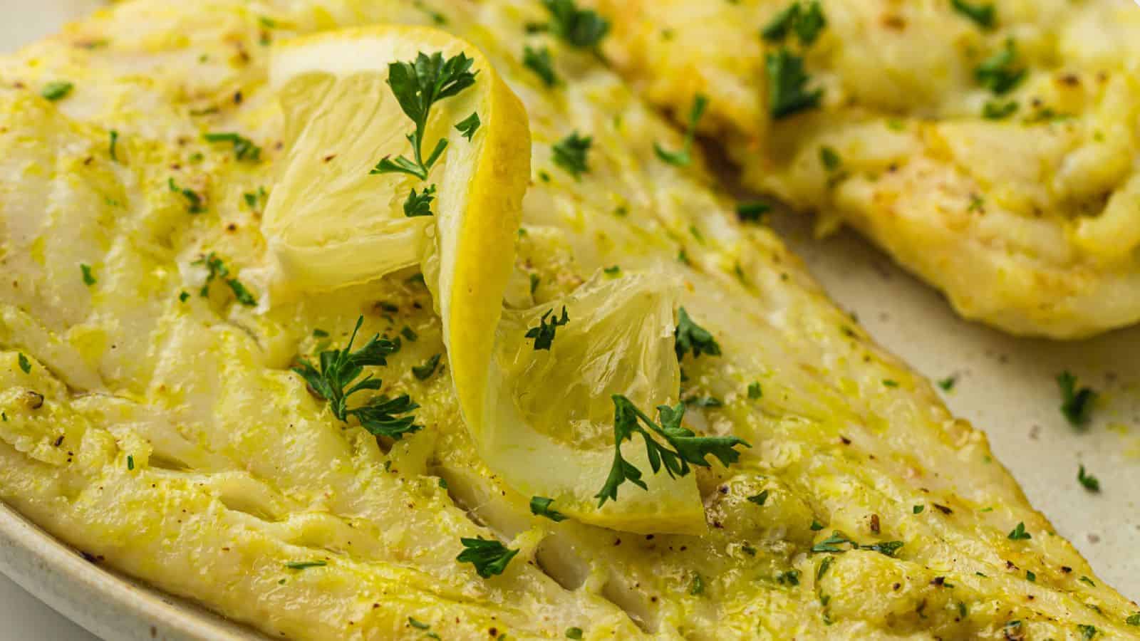 Image of cooked air fryer cod fillets seasoned with herbs and garnished with lemon wedges and parsley on a plate.