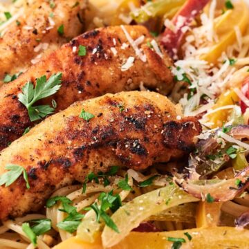 A plate of spaghetti topped with grilled chicken strips and garnished with chopped parsley, bell peppers, and shredded cheese.