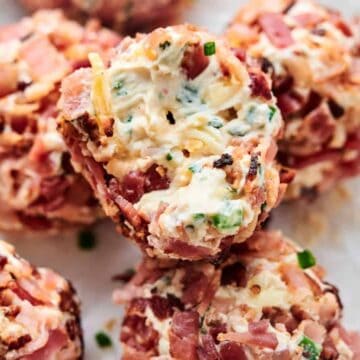 Close-up of several Bacon Jalapeno Popper Cheese Balls wrapped in bacon, stuffed with cheese, and seasoned with herbs and spices, placed on crumpled parchment paper.