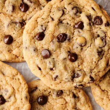 A hand holding a chocolate chip cookie on a cooling rack.