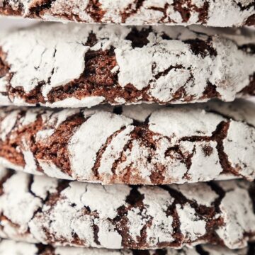 A close-up image shows a stack of four chocolate crinkle cookies covered in powdered sugar, revealing their cracked texture.