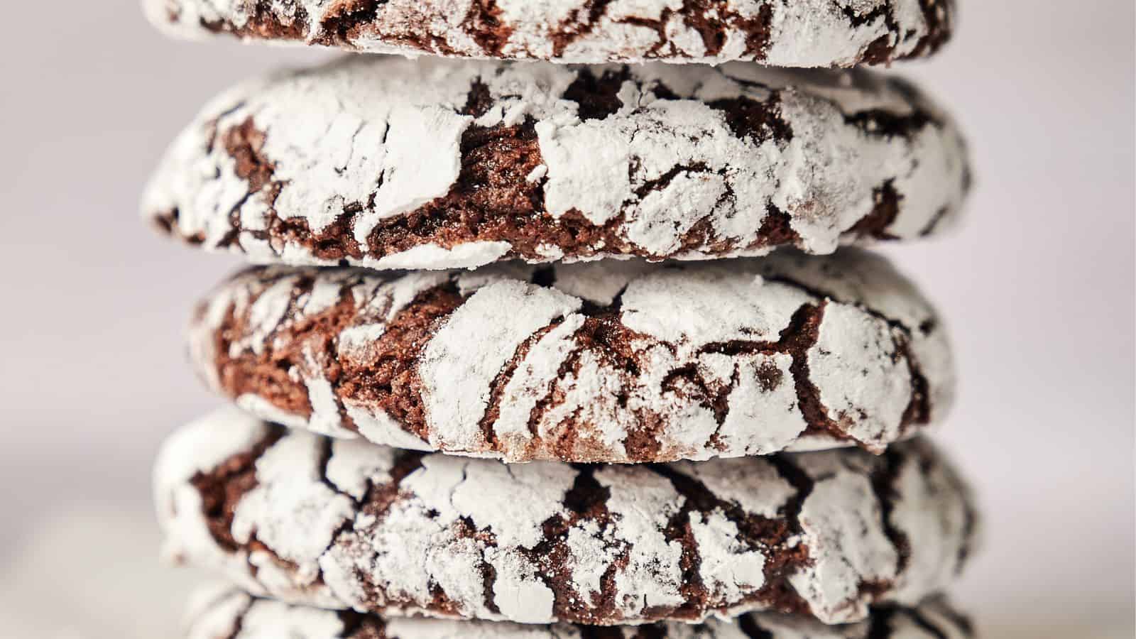 A close-up image shows a stack of four chocolate crinkle cookies covered in powdered sugar, revealing their cracked texture.