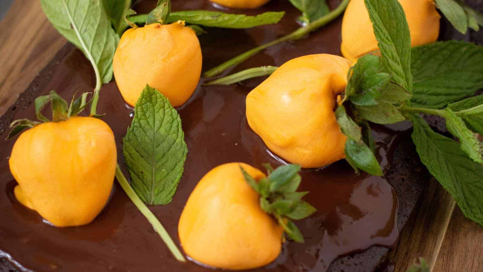 Close-up of five bright orange physalis fruits placed on a chocolate pumpkin patch brownie surface, garnished with fresh green mint leaves.